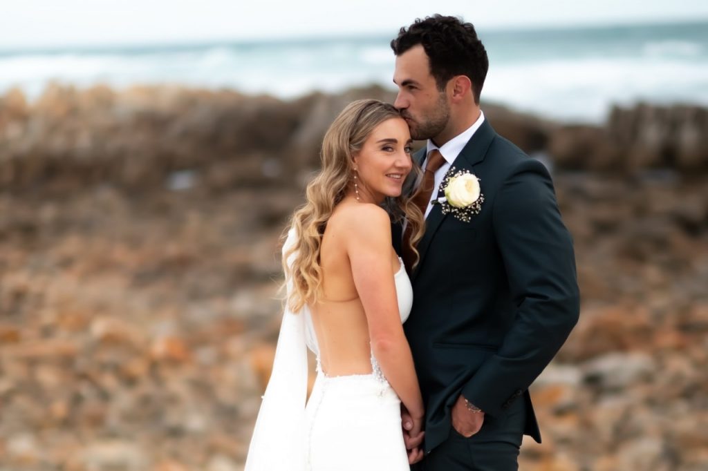 A professional wedding photographer capturing a couple's intimate moment during their outdoor photo session.