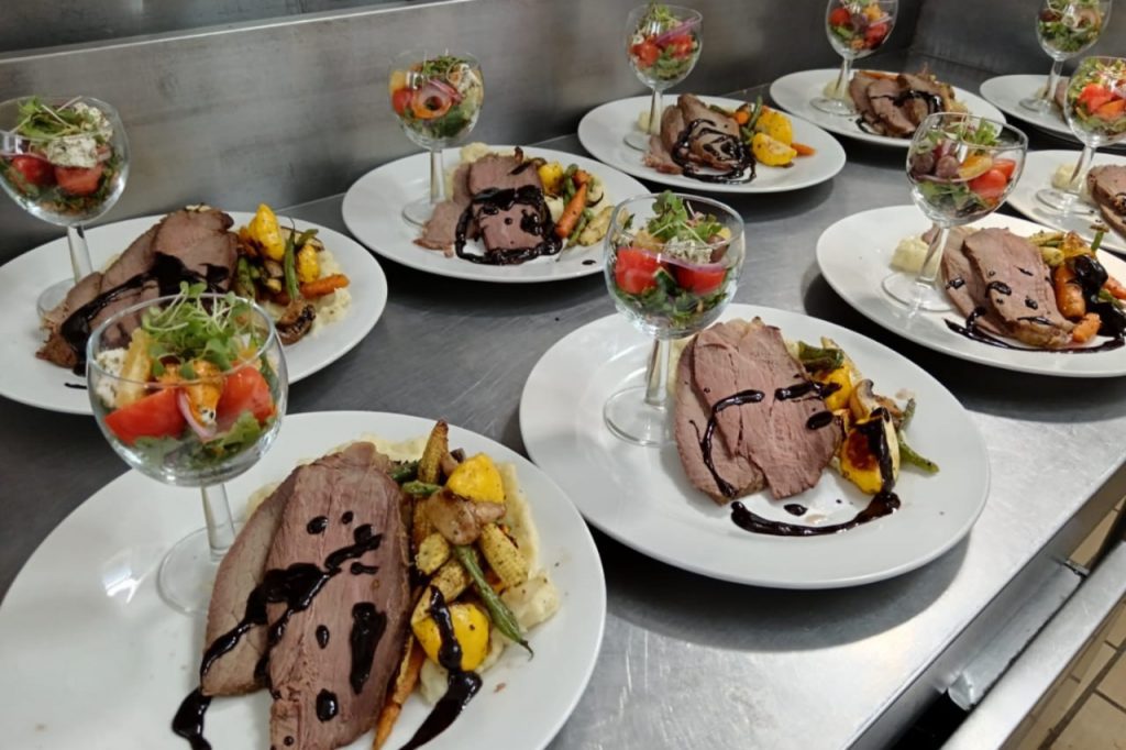 A large spread of plates filled with various meats and colorful vegetables arranged for a meal.