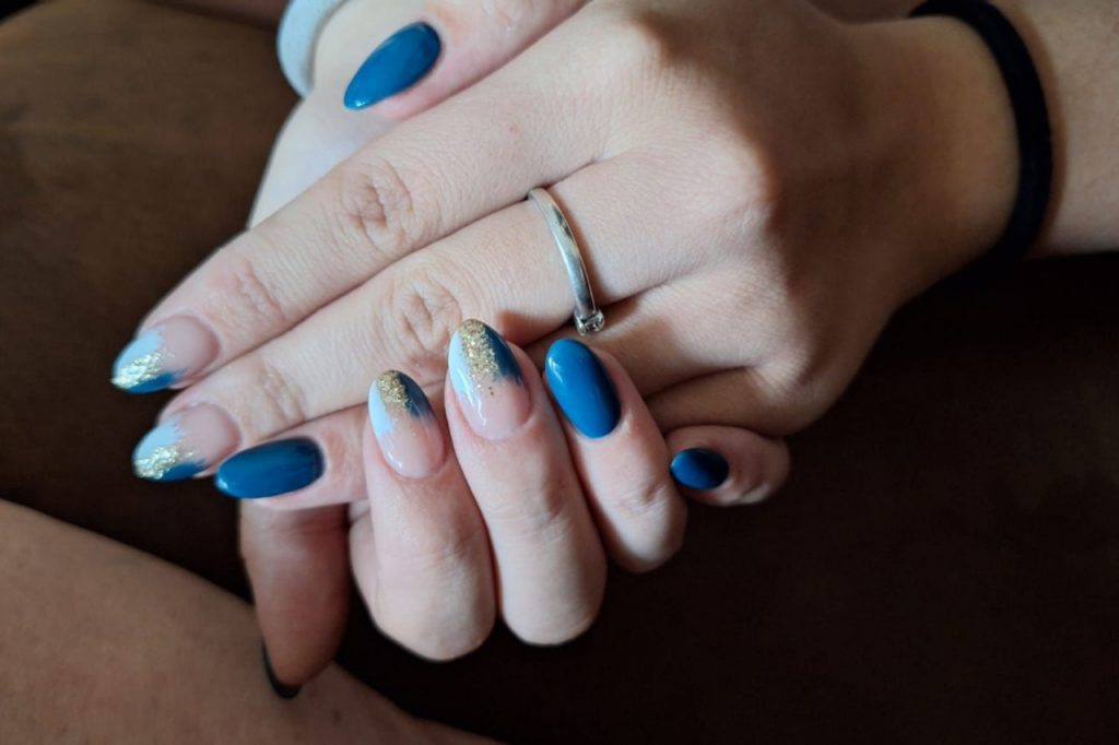 A woman displays her hands with blue and gold manicured nails, showcasing a stylish and artistic nail design.