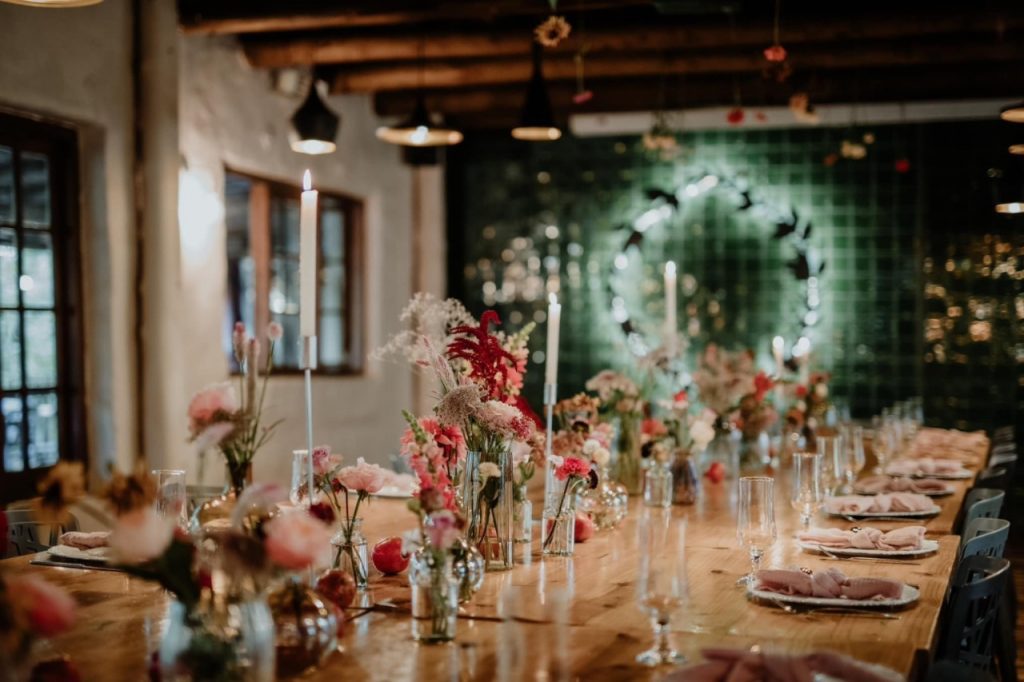 A long dining table adorned with colorful flowers and flickering candles, creating an inviting atmosphere.