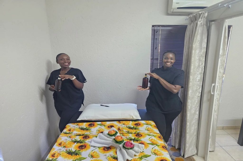 Two women in black shirts stand beside a massage table, ready to assist clients in a calming environment.