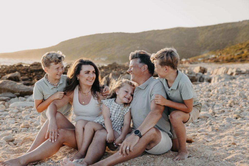 A family gathers on the beach at sunset, surrounded by soft sand and a stunning display of orange and pink hues in the sky.