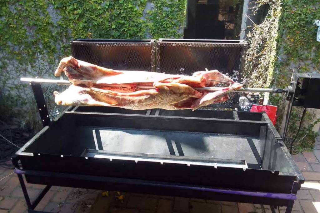 A large piece of meat sizzling on a grill, surrounded by smoke and flames, indicating it's being cooked.
