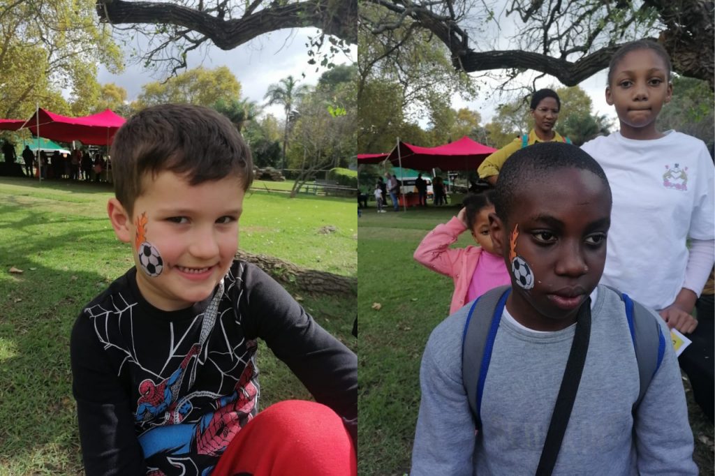 Two children smiling with Spiderman face paint, showcasing vibrant red and blue designs on their cheeks and foreheads.